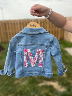 someone holding up a jean jacket with the letter m on it