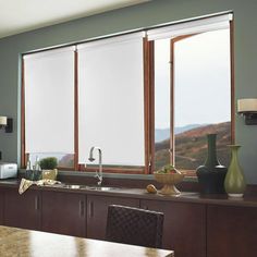 a kitchen with wooden cabinets and white roller shades on the windows over the sink area