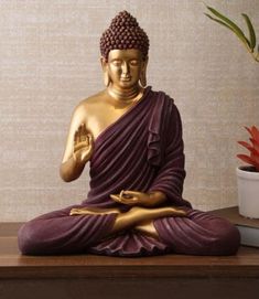 a buddha statue sitting on top of a wooden table next to a potted plant