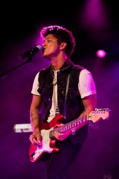 a young man playing an electric guitar in front of a microphone and purple lighting on stage