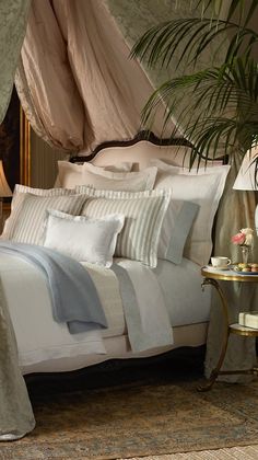 a bed with white sheets and pillows in a bedroom next to a plant on a table