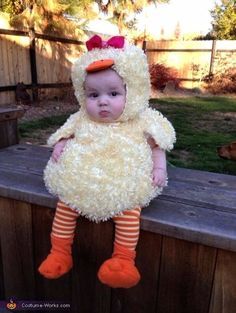 a baby wearing a chicken costume sitting on top of a wooden bench