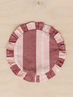 a pink and white striped placemat with ruffles on it, sitting on a wooden surface