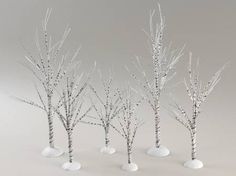 several small white trees with no leaves in the snow on a gray background, set against a plain backdrop