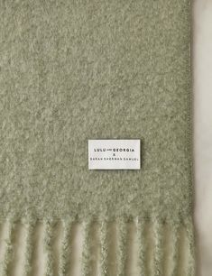 the label is attached to an un - made green wool blanket with ruffled edges