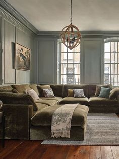 a living room filled with lots of furniture next to two windows and a chandelier hanging from the ceiling