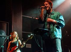 two people on stage singing into microphones and playing instruments in front of an audience