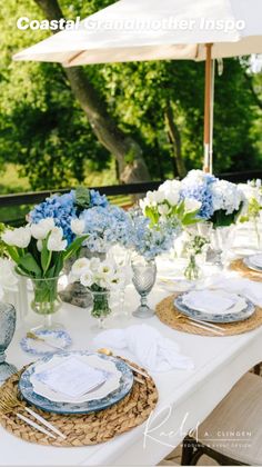 an outdoor table set with blue and white plates, napkins, and vases