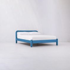 a blue bed frame with white sheets and pillows on the bottom, in front of a plain wall