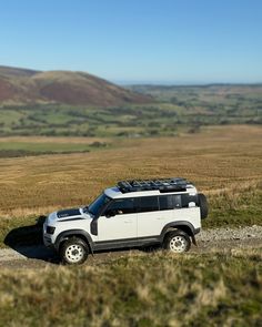 a white jeep parked on the side of a dirt road in an open field with mountains in the background