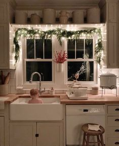 a baby sitting in a kitchen sink next to a window with christmas lights on it