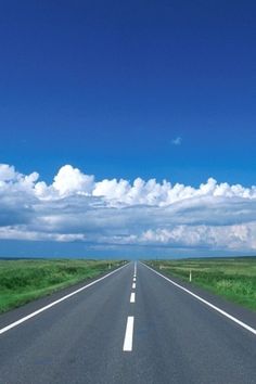 the road is empty and there are clouds in the blue sky above it as well