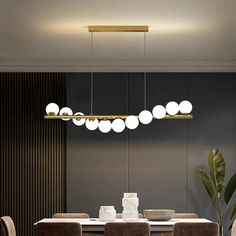 a dining room table and chairs with lights hanging from the ceiling above it, in front of a dark wall