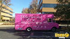 a pink food truck parked in front of a tall building with windows on it's side