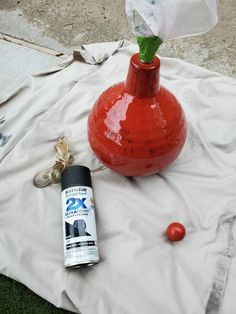 a red vase sitting on top of a white sheet next to a can of paint