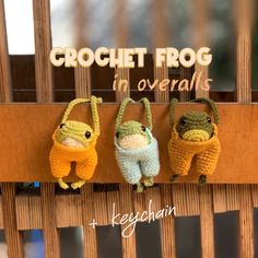 crochet frog in overalls hanging on the side of a wooden slatted fence