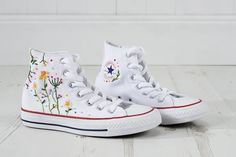 a pair of white converse shoes with flowers painted on the soles and lace detailing