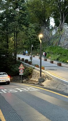 a car is driving down the road near a street sign and some people are walking