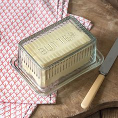 a butter container sitting on top of a wooden table next to a knife and napkin