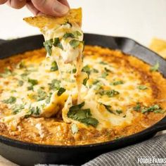 a hand holding a tortilla chip over a skillet filled with cheese and sauce