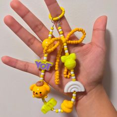 a hand holding a small yellow and white keychain with charms attached to it