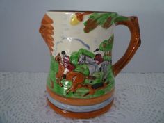 a ceramic mug with horses and trees painted on the inside is sitting on a lace tablecloth