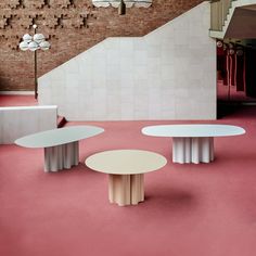 three white tables sitting on top of a pink floor next to a stair case in a building