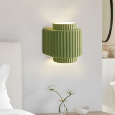 a green lamp on the wall next to a bed and vase with flowers in it