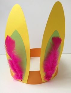 a yellow paper crown with pink feathers on the top and bottom, sitting on a white surface