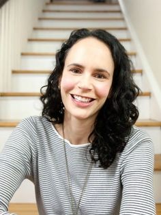 a woman sitting at a table in front of some stairs with her hands on her knees