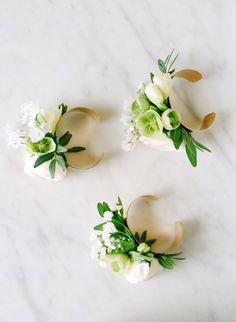 three boutonnieres with white flowers and green leaves on a marble table top