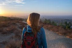 a woman with a backpack is looking at the sunset on top of a hill,