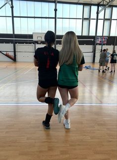 two girls are walking in an indoor basketball court