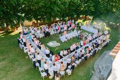 a large group of people sitting around tables in the middle of a field with trees