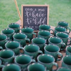 green coffee mugs are sitting on a table with a chalkboard sign in the background