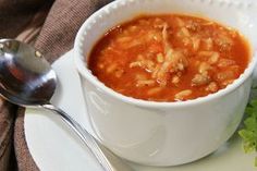 a white plate topped with a bowl of soup and a silver spoon next to it