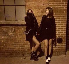 two young women standing next to each other near a brick wall in front of a building