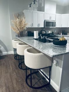 three stools sit at the center of a kitchen island with granite countertops and white cabinets