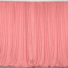 an orange cat sitting on top of a wooden floor next to a pink curtained wall