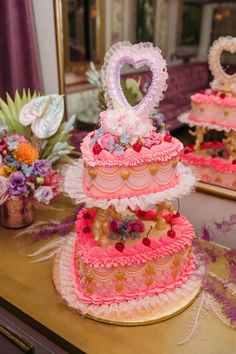 three tiered cake with hearts and flowers on top sitting on a table in front of a mirror