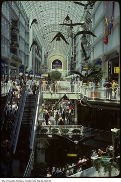 an indoor mall filled with lots of people and birds flying above the escalators