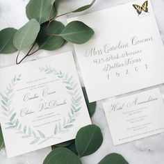 the wedding stationery is laid out with greenery and calligraphy on top of it