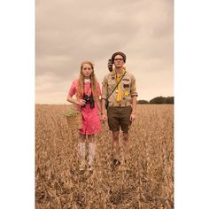 two people standing in the middle of a wheat field, one holding a camera and the other carrying a basket