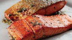 two pieces of salmon on a plate with seasoning sprinkled on top and another piece of fish in the background