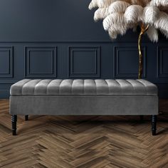 a grey bench sitting on top of a wooden floor next to a palm tree in a room