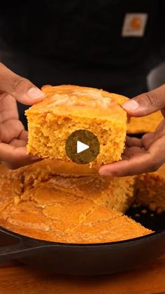 two hands holding a piece of cornbread in a skillet