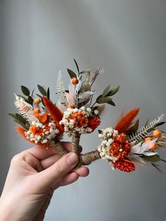 a person holding flowers in their hand with orange and white blooms on the stems,