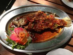 a silver plate topped with fish covered in sauce and garnish next to a flower