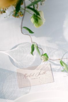 a white table cloth with a place card and some flowers on top of the table