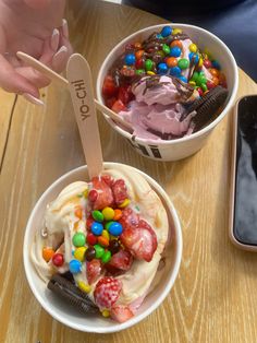 two bowls filled with ice cream and candy on top of a wooden table next to an iphone